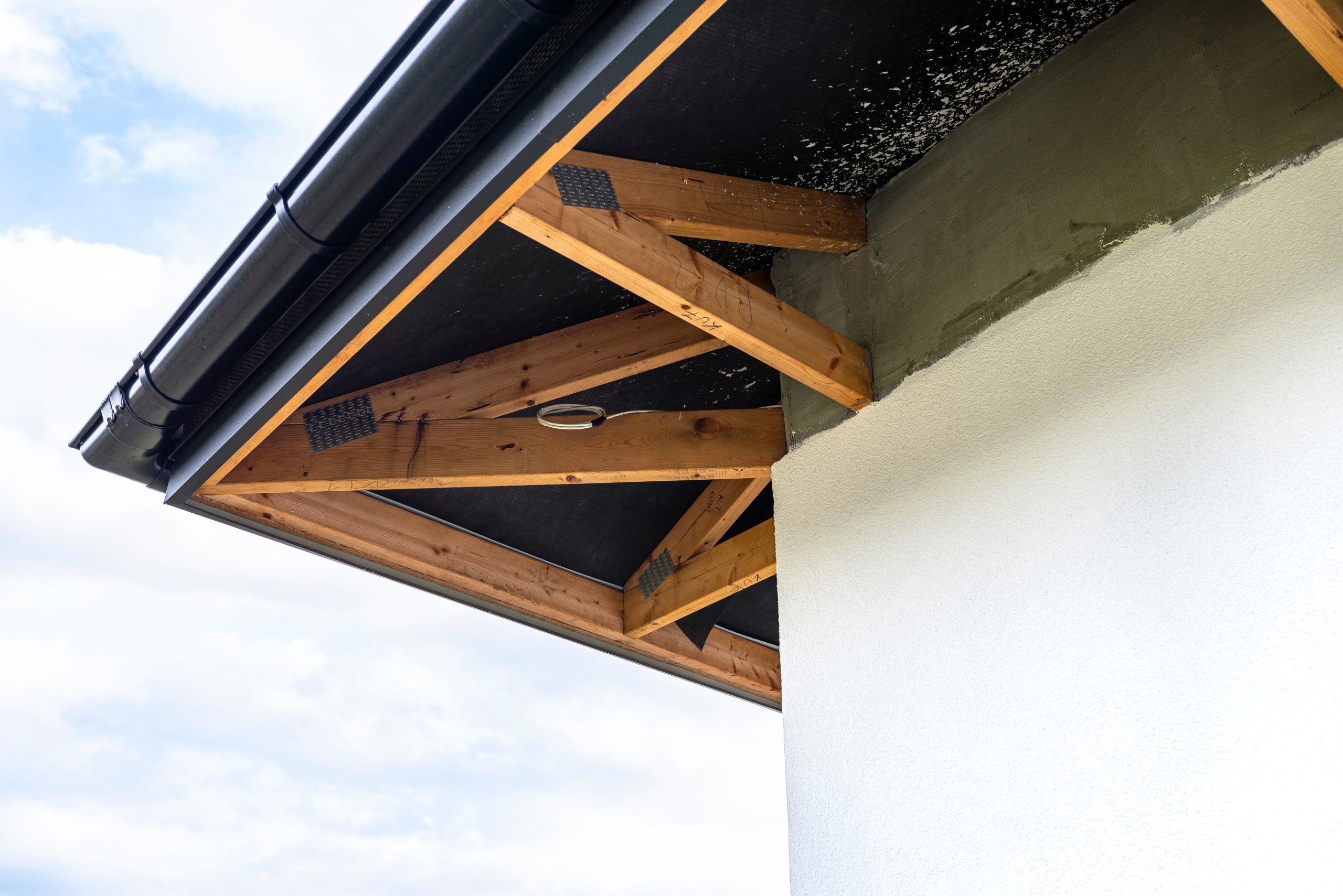 A newly applied layer of white silicone plaster on the wall of the house, visible roof trusses and a gutter. Factors that impact the price of a new roof in Fort Worth